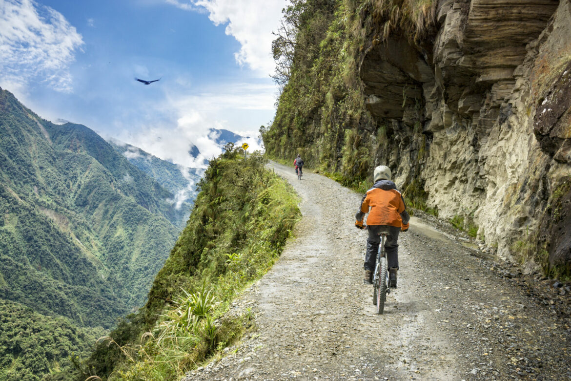 Bike adventure travel photo. Bike tourists  ride on the "road of death"  downhill track  in Bolivia. In the background sky circles a condor over the scene.