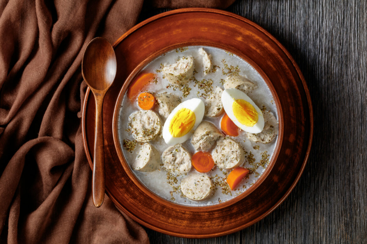 Zurek polish fermented rye soup with traditional polish white kielbasa or sausage with marjoram, hard-boiled eggs served on a clay bowl with a wooden spoon, on a dark wooden background, top view